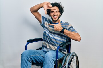 Poster - Handsome hispanic man sitting on wheelchair smiling making frame with hands and fingers with happy face. creativity and photography concept.