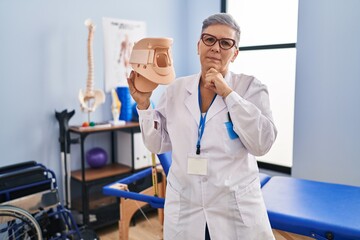 Sticker - Middle age woman holding cervical neck collar serious face thinking about question with hand on chin, thoughtful about confusing idea