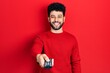 © Krakenimages.com - Young arab man with beard holding television remote control smiling and laughing hard out loud because funny crazy joke.