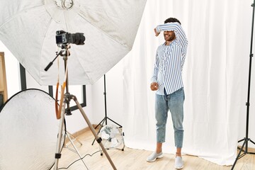 Canvas Print - Arab young man posing as model at photography studio covering eyes with arm smiling cheerful and funny. blind concept.