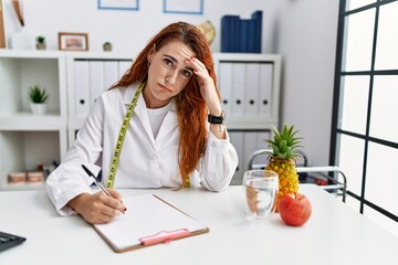 Sticker - Young redhead woman nutritionist doctor at the clinic worried and stressed about a problem with hand on forehead, nervous and anxious for crisis