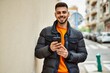 © Krakenimages.com - Handsome hispanic man with beard smiling happy and confident at the city wearing winter coat using smartphone