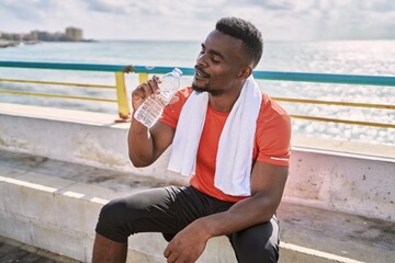 Young african american man wearing sportswear holding water bottle at seaside