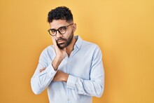 Hispanic Man With Beard Standing Over Yellow Background Thinking Looking Tired And Bored With Depression Problems With Crossed Arms.
