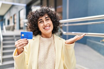 Sticker - Young brunette woman with curly hair holding credit card celebrating achievement with happy smile and winner expression with raised hand