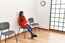 Young Latin Woman Reading Document Sitting On Chair At Waiting Room