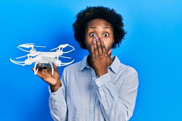 Wall Mural - Young african american woman holding drone covering mouth with hand, shocked and afraid for mistake. surprised expression