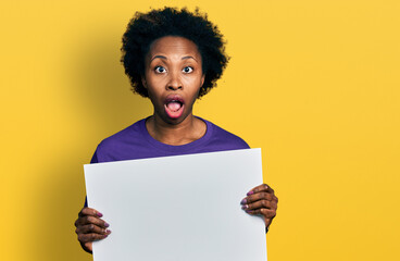 Poster - African american woman with afro hair holding blank empty banner afraid and shocked with surprise and amazed expression, fear and excited face.