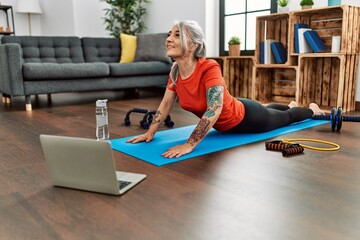 Middle age grey-haired woman smiling confident having online stretching class at home