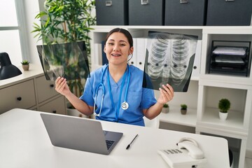 Canvas Print - Young latin doctor woman holding x-ray smiling and laughing hard out loud because funny crazy joke.