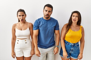 Canvas Print - Group of young hispanic people standing over isolated background in shock face, looking skeptical and sarcastic, surprised with open mouth