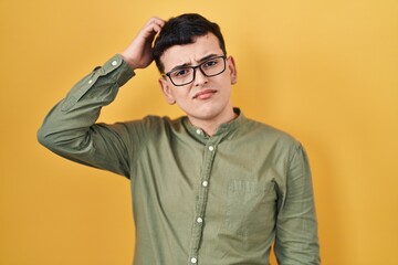 Wall Mural - Non binary person standing over yellow background confuse and wonder about question. uncertain with doubt, thinking with hand on head. pensive concept.