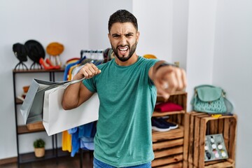 Wall Mural - Young handsome man with beard holding shopping bags at retail shop pointing displeased and frustrated to the camera, angry and furious with you