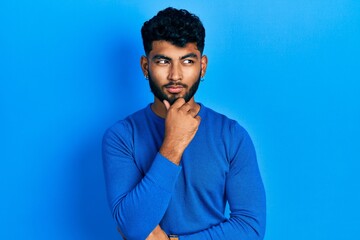 Canvas Print - Arab man with beard wearing casual blue sweater with hand on chin thinking about question, pensive expression. smiling with thoughtful face. doubt concept.