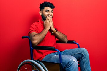 Wall Mural - Arab man with beard sitting on wheelchair laughing and embarrassed giggle covering mouth with hands, gossip and scandal concept