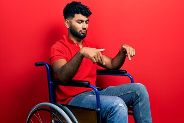 Sticker - Arab man with beard sitting on wheelchair pointing down looking sad and upset, indicating direction with fingers, unhappy and depressed.