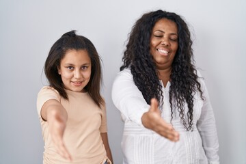 Sticker - Mother and young daughter standing over white background smiling friendly offering handshake as greeting and welcoming. successful business.