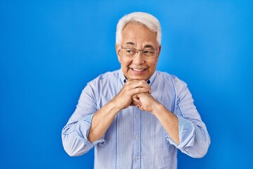 Poster - Hispanic senior man wearing glasses laughing nervous and excited with hands on chin looking to the side