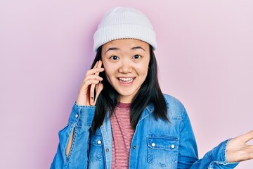 Wall Mural - Young chinese girl having conversation talking on the smartphone celebrating achievement with happy smile and winner expression with raised hand