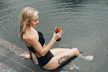 Wall Mural - The beautiful and stylish blond woman relaxing in the pool with a cocktail in summer