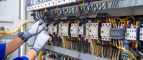 Electricity and electrical maintenance service, Engineer hand holding AC voltmeter checking electric current voltage at circuit breaker terminal and cable wiring main power distribution board.