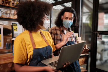 Wall Mural - Two young cafe barista partners and entrepreneur work with face mask in coffee shop, waiting for customers order in new normal lifestyle service, SME business impact from COVID19 pandemic quarantine.