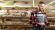 © Andrii Lysenko - Confident supermarket clerk working with a digital tablet. Young handsome supervisor with tablet pc in the mall, background of bread shelves, technology and work concept. banner
