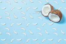 Two Halves Of A Coconut Located In The Upper Corner Of The Frame Surrounded By Coconut Chips, Coconut Slices, On A Blue Background. Coconut Pattern.