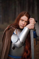 Portrait red-haired girl in medieval knight's armor in summer forest