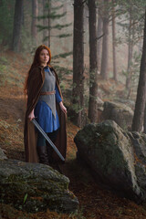 Wall Mural - Red-haired girl in armor and raincoat in forest. Historical concept