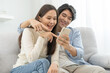 Happy couple love at home,beautiful two asian young spending good time together,bonding to each other and smiling romantic on sofa in living room while man embrace woman using smartphone, mobile phone