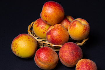 Sticker - Apricots in a small basket on a black background. Ripe fresh fruits.