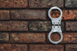 Closed handcuffs hang on a brick wall.