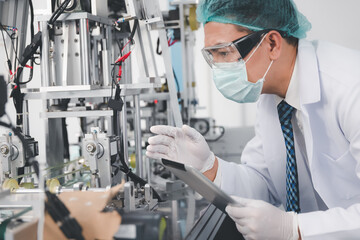 Doctor engineer or scientist in face mask using computer tablet working with medical mask production machine factory