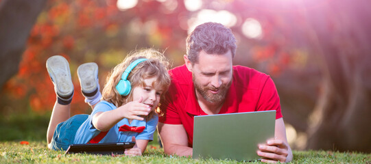 Wall Mural - Banner of father on son school boy with laptop study online lying on grass, father and son use modern communication technology in park. family blog.