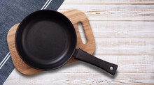 Black Fry Pan And Board With Napkin On Wooden Table. Top View Mockup