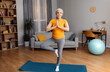 Yoga practice on retirement. Calm senior lady standing in tree pose, keeping balanced, exercising on yoga mat at home