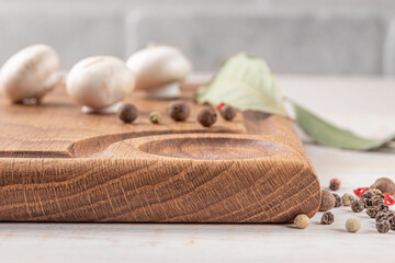 Wall Mural - square wooden cutting board of dark color with edging. mushrooms and spices on a white background. mockup with copy space for text, side view, close-up