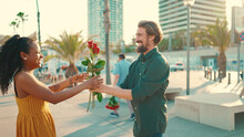 Close-up Of Young Happy Man And Woman Joyfully Hugging When Meeting On The Embankment, Man Gives Girl A Bouquet Of Red Roses. Closeup, Joyful Date Of A Young Interracial Couple.