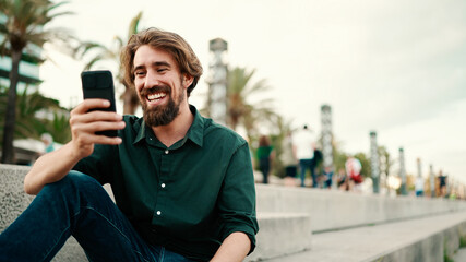 Close-up portrait of a man with a beard recording a voice message on the embankment background. Closeup of a young hipster male using a mobile phone