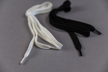 Two flat laces opposite the gray background. White and black. Laces with loop and tied knot. Close-up. Selective focus.