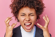 Close Up Shot Of Irritated Woman With Curly Hair Screams And Gestures Angrily Being Annoyed Shouts Furiously Feels Enraged And Aggressive Poses Indoor Against Pink Background. Negative Emotions