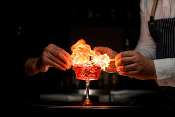 wonderful view on crystal goblet with cocktail that bartenders impressively sets to fire