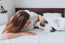 Happy Young Woman With Cat In Bed At Home. In Cold Weather, The Pet Warms Up Under A Blanket. Pet Friendly And Grooming Concept. Stray Kitten Sleep On Bed. Cozy Home Background, Morning Bedtime.
