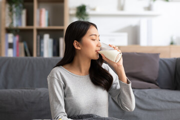 Healthy Young Asian woman Drinking milk with calcium for strong bone at home. Smiling indian woman holding soy milk on glass enjoy with nutrition wellness life.Wellness with natural milk fresh Concept