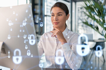 Wall Mural - Attractive businesswoman in white shirt at workplace working with laptop to defend customer cyber security. Concept of clients information protection. Padlock hologram over office background.