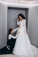 Wall Mural - dressmaker helping the bride to put her wedding dress on in clothes shop.