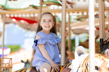 Adorable little girl in blue dress at amusement park having a ride on the merry-go-round