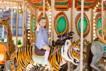 Adorable little girl in blue dress at amusement park having a ride on the merry-go-round