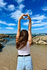 a cheerful teen girl stands against the backdrop of the ocean in a beautiful dress, she raised her hand, you can advertise a travel agency trip to Portugal 